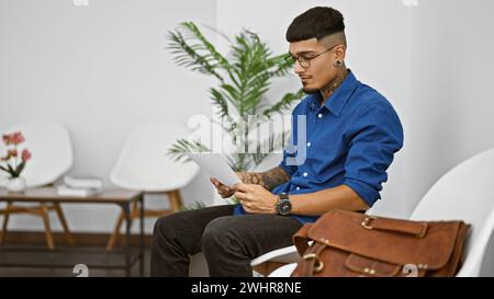 Ein hübscher lateinischer Mann, ein Porträt eines jungen tätowierten Profis, der seine Ideen zweifelt, während er sich auf das Lesen eines Dokuments konzentriert, während er in einer Wartezeit sitzt Stockfoto