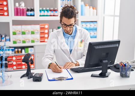 Junger hispanischer Apotheker, der auf einem Dokument in der Apotheke schreibt Stockfoto