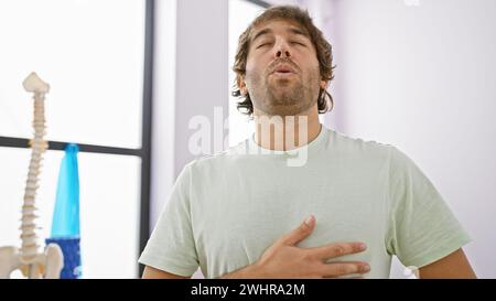 Ein junger Mann mit Bart atmet tief in einer hell beleuchteten Reha-Klinik aus und zeigt Entspannung und Wohlbefinden. Stockfoto