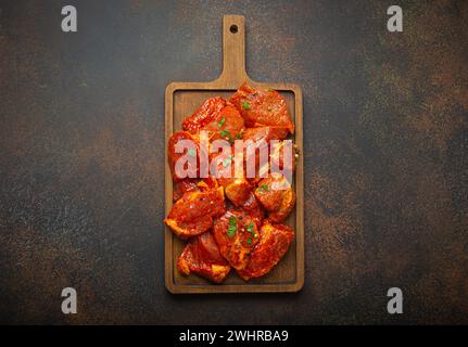 Rohe, ungekochte, geschnittene Schweinefleisch-Stücke, mariniert mit Gewürzen und Petersilie auf hölzernem Schneidebrett, Blick von oben auf dunklem rustikalem Backgr Stockfoto