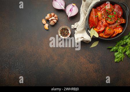 Kochen Sie herzhaften Fleischeintopf. Rohe, nicht gekochte, gehackte Fleischstücke, mariniert mit Gewürzen und Petersilie in einem schwarzen Auflauftopf Stockfoto