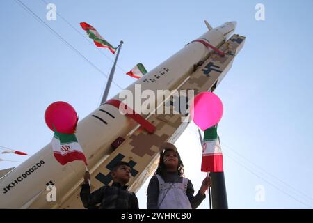 Teheran, Iran. Februar 2024. Ein iranischer Junge und ein iranisches Mädchen halten iranische Flaggen neben den iranischen Raketen auf dem Azadi-Platz in Teheran, während sich Menschen zum 45. Jahrestag der islamischen Revolution in Teheran versammeln. Der Iran bezeichnete am 11. Februar 2024 den 45. Jahrestag der Islamischen Revolution von 1979, inmitten von Spannungen, die den Nahen Osten über den fortgesetzten Krieg Israels gegen die Hamas im Gazastreifen ergriffen haben. Der iranische Präsident Ebrahim Raisi verurteilte den Erzfeind Israel und verlangte seine Ausweisung aus den Vereinten Nationen. (Kreditbild: © Rouzbeh Fouladi/ZUMA Press Wire) NUR REDAKTIONELLE VERWENDUNG! Nicht Stockfoto