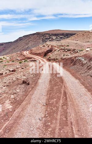Eine gewundene Feldstraße schlängelt sich durch eine zerklüftete Wüstenlandschaft unter einem blauen Himmel und vermittelt ein Gefühl von Abenteuer und Isolation. Stockfoto