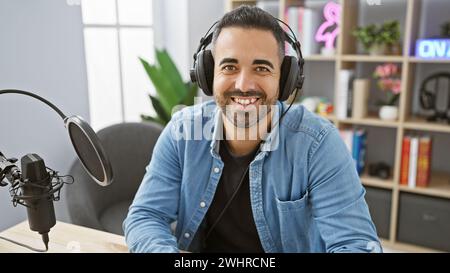 Hübscher Mann mit Kopfhörern, die in einem modernen Radiostudio lächeln. Stockfoto