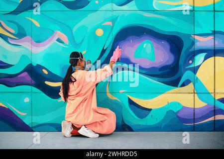 Straßenkünstlerin in Atemschutzmaske, die bunte Graffiti an die Wand malt Stockfoto