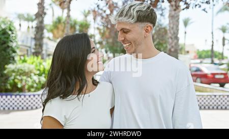 Ein lächelndes Paar umarmt sich in einem sonnigen Park, der von Grün und Palmen umgeben ist. Stockfoto