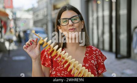 Wunderschöne hispanische Frau, die fröhlich knusprige, leckere Chips auf einem Stock in der takeshita Street, tokio isst - Reisende Junk Food Liebhaber, Sportbrille Stockfoto