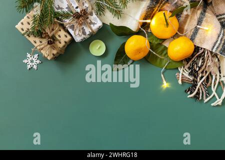 Winterkomposition mit Tannenzweigen, Geschenk, Schal und Mandarinen auf grünem Hintergrund. Gemütliche Winterstimmung. Blick von oben. Co Stockfoto