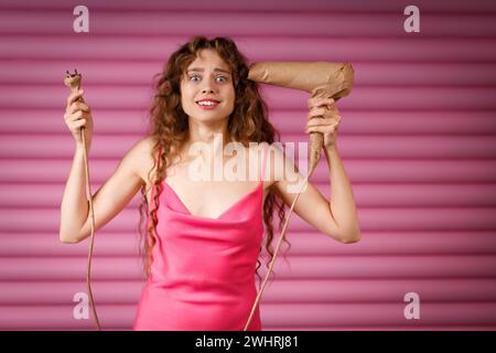 Junge positiv lächelnde Frau erhält Überraschungsgeschenk Handgriff Haartrockner in rustikalem Beige Bastelpapier gewickelt. Black Friday Conce Stockfoto