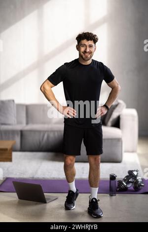 Athlet man trainiert hart in leerem Fitnessstudio oder zu Hause vor dem Laptop. Selbstisolierte und motivierte Aufwärmübungen für junge Männer Stockfoto
