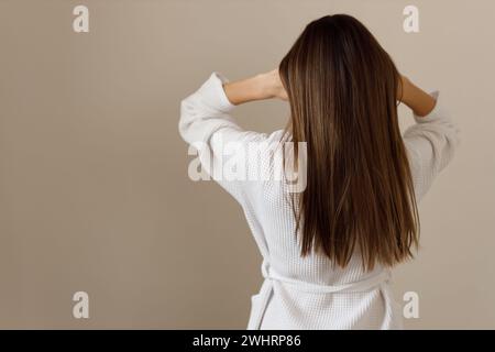 Junge Frau mit gesunden langen glatten Haaren im weißen Bademantel, Rückansicht. Hygiene, Frische, Reinigung nach dem Duschen. Wirkung von Co Stockfoto