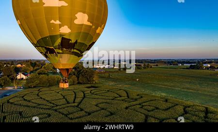 Luftaufnahme eines Golden Hot Air Balloons, der gerade gestartet wurde und mit einem Maislabyrinth über ein Feld schwingt Stockfoto