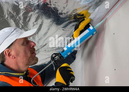 Ein Arbeiter in Weste, Kappe und Handschuhen verwendet eine Heißluftpistole. Stockfoto