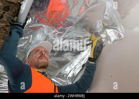 Der Bauarbeiter hält eine Dampfsperre in der Hand - Vorbereitung für die Befestigung. Stockfoto