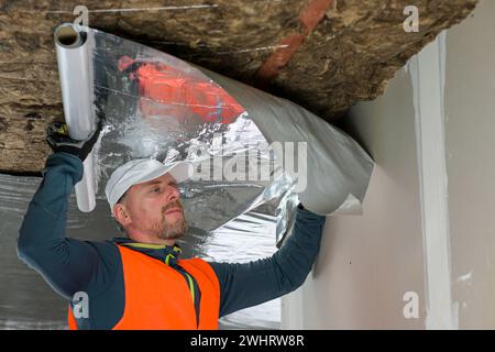 Der Bauarbeiter hält eine Dampfsperre in der Hand - Vorbereitung für die Befestigung. Stockfoto