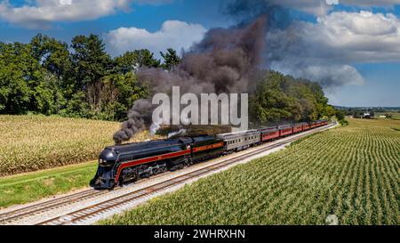 Aus der Vogelperspektive eines restaurierten antiken Dampfeisenzugs, der durch die Landschaft fährt, an Maisfeldern vorbeifährt und S bläst Stockfoto