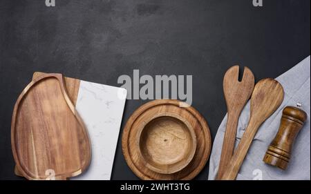 Leere Schüssel und Holzlöffel auf einem schwarzen Tisch, Blick von oben Stockfoto