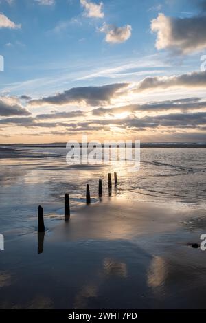 Eine Reihe von Polen am Strand, die unter einem dramatischen Sonnenuntergang ins Meer führt Stockfoto