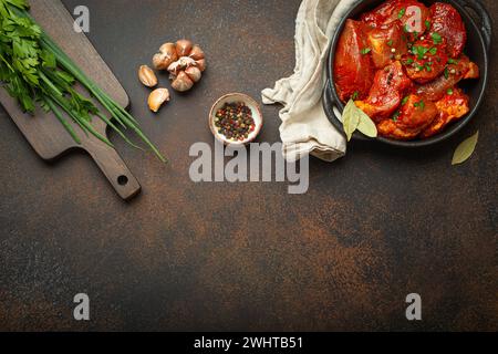 Kochen von Fleischeintopf. Rohe, nicht gekochte, gehackte Fleischstücke, mariniert mit Gewürzen und Petersilie in schwarzer Auflaufform, Blick von oben, c Stockfoto