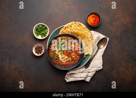 Traditionelles indisches Punjabi-Gericht Dal Makhani mit Linsen und Bohnen in schwarzer Schüssel serviert mit Naan-Fladenbrot, frischem Koriander und Stockfoto