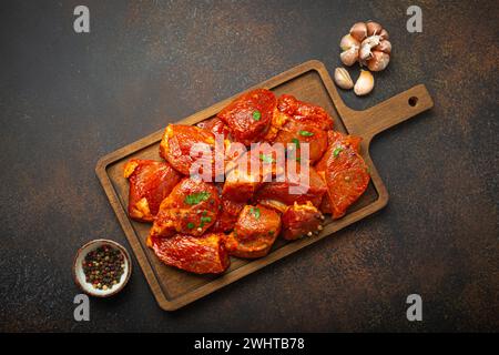 Rohe, ungekochte, geschnittene Schweinefleisch-Stücke, mariniert mit Gewürzen und Petersilie auf hölzernem Schneidebrett, Blick von oben auf dunklem rustikalem Backgr Stockfoto