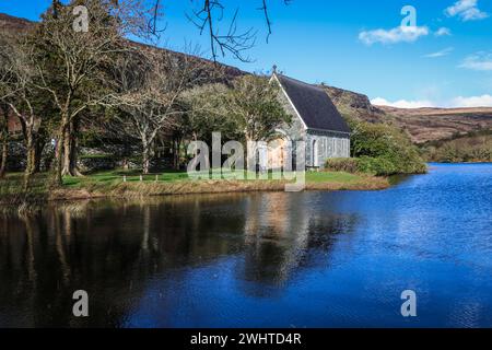 Zeitlose Ruhe in Gougane Barra, County Cork, Irland – wo das Wasser anmutig um eine historische Kapelle fließt und die Essenz der Ruhe einfängt Stockfoto