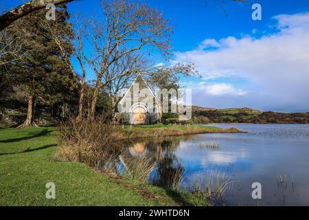 Zeitlose Ruhe in Gougane Barra, County Cork, Irland – wo das Wasser anmutig um eine historische Kapelle fließt und die Essenz der Ruhe einfängt Stockfoto