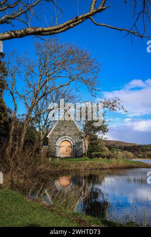 Zeitlose Ruhe in Gougane Barra, County Cork, Irland – wo das Wasser anmutig um eine historische Kapelle fließt und die Essenz der Ruhe einfängt Stockfoto