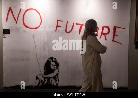 Moskau, Russland. Februar 2024. Eine Frau steht vor dem Gemälde „No Future“, das während einer Ausstellung zu Ehren des englischen Straßenkünstlers Banksy in Moskau, Russland, ausgestellt wird. Unter dem Titel „Find Banksy“ und im VDNKH-Pavillon Nr. 21 gehalten, enthält es Kopien der Originalwerke von Banksy Stockfoto