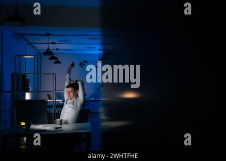 Fernsicht auf müde junge Männer macht eine Pause von der Arbeit am Computer am Arbeitsplatz, macht Sport und streckt die Hände nach oben. Geschäftsmann dehnen Stockfoto