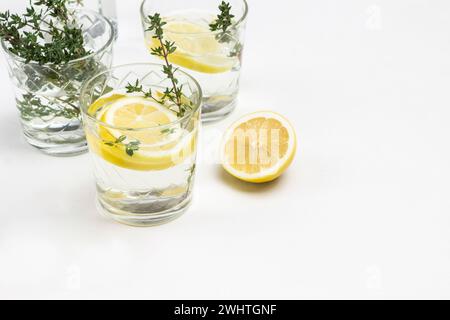 Zitronengetränk im Glas. Thymianzweige in Glas. Zitronen auf dem Tisch und in der Keramikschale. Nahaufnahme. Weißer Hintergrund. Draufsicht. Stockfoto