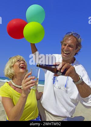 Senioren, Paar am Strand auf Ibiza, Ballons, Champagner, Feierlichkeiten, Urlaubsfreuden Stockfoto