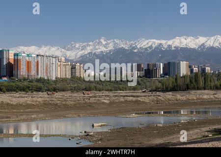 Speicherreservoir Sayran-See, Almaty, Kasachstan. Leerer City Sandstrand mit entwässertem Teich. Wohnhäuser und hohe schneebedeckte Montage Stockfoto