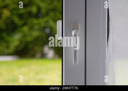 Metall-Kunststoff-Fenster mit weißem Griff und Vorhang. Stockfoto