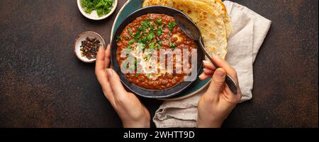 Weibliche Hände halten eine Schüssel und essen traditionelles indisches Punjabi-Gericht Dal Makhani mit Linsen und Bohnen serviert mit Naan Flat Stockfoto