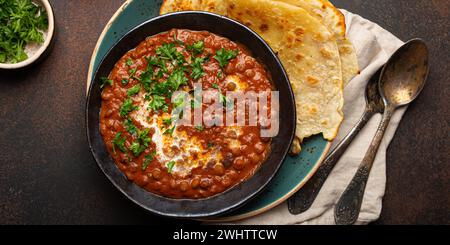 Traditionelles indisches Punjabi-Gericht Dal Makhani mit Linsen und Bohnen in schwarzer Schüssel serviert mit Naan-Fladenbrot, frischem Koriander und Stockfoto