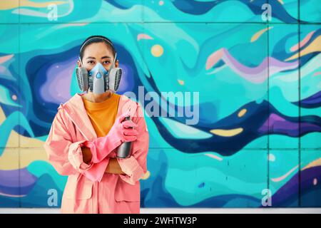 Graffiti-Künstlerin Malerin in Atemschutzmaske, die neben der Wand steht und ihre Gemälde in die Kamera blickt Stockfoto