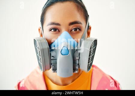 Nahporträt einer jungen Frau in Atemschutzmaske, die auf weißem Hintergrund in die Kamera schaut Stockfoto