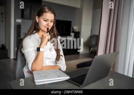 Junge Frau, die ihr Notebook am Arbeitsplatz zu Hause nutzt, Notizen schreibt, Schülerinnen lernen und Online-Webinare anschauen oder Audiokurse hören, e-Learning Stockfoto