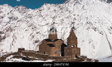 Die historische Kirche mit klassischer Architektur steht in krassem Kontrast zu den schroffen, verschneiten Bergen unter klarem Himmel. Stockfoto