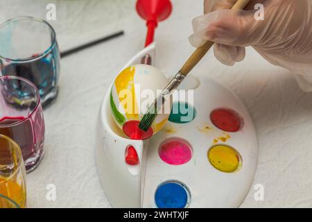 Kinderhand in Einweghandschuhen zum Färben eines Ostereis mit Speisefarben. Stockfoto