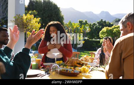 Fröhliche, vielfältige männliche und weibliche Freunde servieren Thanksgiving-Festmahlzeiten im sonnigen Garten Stockfoto