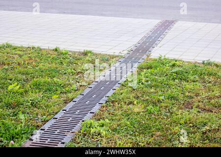 Langer Regenabfluss auf Gras und Gehsteig aus nächster Nähe Stockfoto