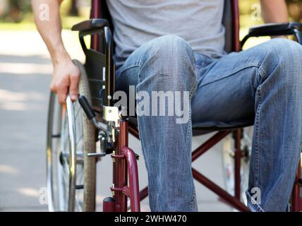 Behinderter Mann, der seinen Rollstuhl in Parknähe benutzt Stockfoto