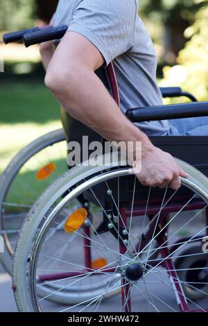 Behinderter Mann, der seinen Rollstuhl in Parknähe benutzt Stockfoto