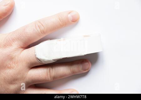 Die Hand eines Mannes mit einem gebrochenen Finger und einer Schiene auf einem gebrochenen Finger auf einem weißen Hintergrund, ein gebrochener Finger, Verletzung, Unfall, ein Mann brach sich die Flosse Stockfoto