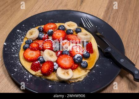 Frühstück mit Pfannkuchen mit Obst, Frühstück Erdbeeren Bananen und Heidelbeeren mit Ahornsirup und Puderzucker, glutenfrei Stockfoto