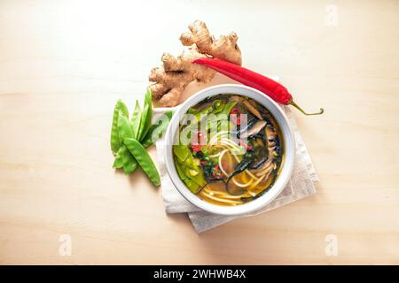 Vegetarische Suppe, in asiatischer Art mit Gemüse, Nudeln, Miso, Nori-Algen, Ingwer und Chili in einer Schüssel auf einem Holztisch zubereitet Stockfoto