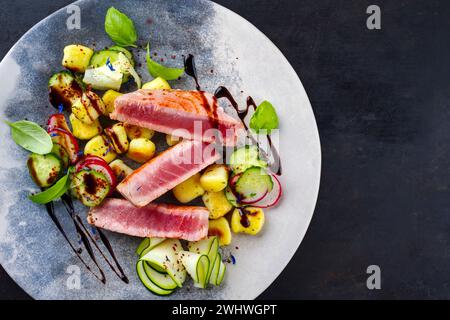 Traditionelles italienisches gebratenes Thunfischsteak mit Gnocchi und Gurkenscheiben serviert als Blick von oben auf einem nordischen Teller mit Kopie Stockfoto