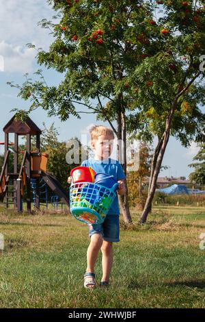 Ein trauriger kleiner Junge mit seiner Tasche voller bunter Spielzeuge auf dem Spielplatz in der Nähe des rowan Tree. Stockfoto